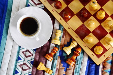 Top view on chess game, felled pieces and cups of strong invigorating black coffee in a white cup on a saucer. Flat lay