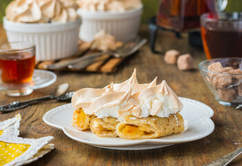 Dessert, thin pancakes with apple filling baked under meringue on a white plate on a green concrete background. Pancake recipes, international pancake day.