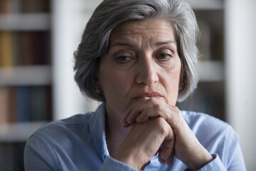 Fototapeta na wymiar Close up worried middle-aged woman deep in sad thoughts, troubled with business or personal life concerns. Frustrated businesswoman thinks seated at workplace, feel distressed looks helpless concept