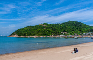 Fototapeta premium A couple sit on the beach watching a beautiful sea under blue sky on a sunny day in Hong Kong Peng Chau Island