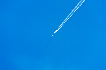 An air plane fly over the clear blue sky with contrail behind.