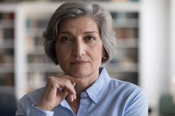 Close up head shot beautiful grey-haired woman touch chin with hand staring at camera, looks...