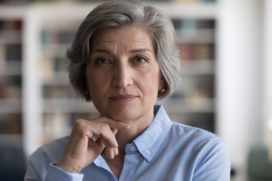 Close up head shot beautiful grey-haired woman touch chin with hand staring at camera, looks confident and serious, having elegant style, attractive appearance. Mature businesswoman portrait concept