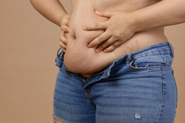 Fat female adult showing fat belly pressing on it with hands wearing blue jeans on beige...