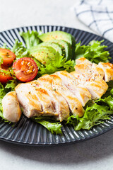 Grilled chicken breast salad with avocado and cherry tomatoes on gray plate. Healthy diet food concept.