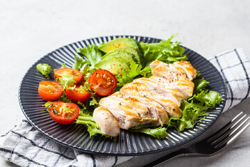 Grilled chicken breast salad with avocado and cherry tomatoes on gray plate. Healthy diet food concept.