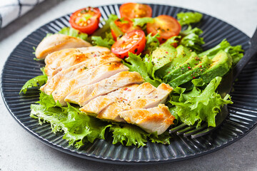 Grilled chicken breast salad with avocado and cherry tomatoes on gray plate. Healthy diet food concept.