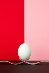 Egg balanced on two metal forks, multicolored background. Easter concept.