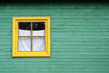 Obraz na płótnie Canvas Wooden window with yellow frame on the green wall of the wooden house.