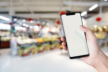 Closes-up hand holding mobile screen smartphone with supermarket blurred background.