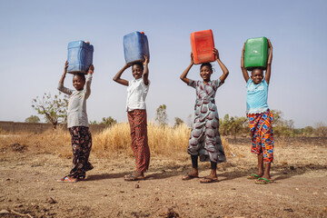 Four young girls,in a rural african village,transporting clean water in heavy plastic cans.