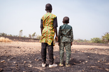 Two african children hopelessly standing in front of a burnt wheat field.Climate crisis,global...