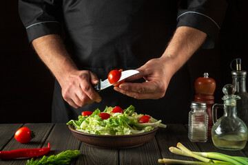 A professional chef prepares a vegetable salad in the restaurant kitchen. Cutting a fresh tomato for a vitamin salad with a knife.