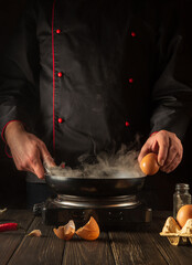 The chef tries to break an egg on a frying pan to make delicious breakfast. Working environment in the kitchen. Menu idea for a restaurant or hotel