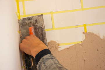 Hand with putty knife repair damaged wall