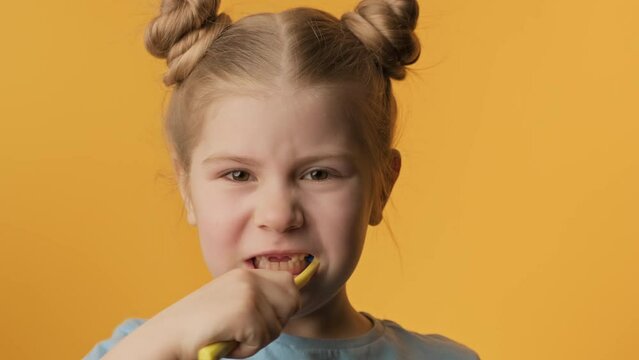Little girl brushing teeth at yellow background. Children daily healthcare routine. Cute girl brush her teeth with toothbrush. Close-up in 4K, UHD