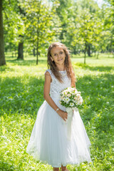 Fototapeta na wymiar Little girl in a white dress with a bouquet of flowers in a summer park.