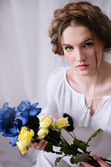 Caucasian Ukrainian woman sitting in the studio in a dress and yellow-blue flowers on a white background during the war. Concept - Stop the war in Ukraine.