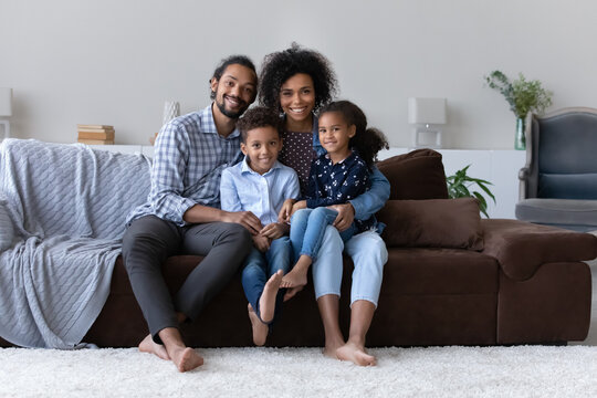 Happy perfect young Black family with two little sibling kids home portrait. Cheerful attractive couple of parents sitting on couch, holding preschool son and daughter on lap