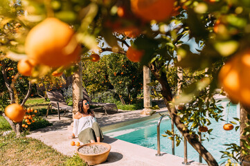 Junge Frau im Urlaub am Pool inmitten von Orangen Bäumen in Spanien