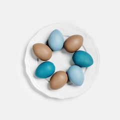 Dyed Easter eggs pastel colors blue, beige on round white plate. Happy Easter holiday concept, celebration food, decorated chicken egg, neutral trendy colored card. Top view table