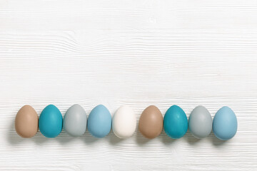 Easter eggs pastel colors lined up row on white wooden background with copy space. Easter celebration concept, card with dyed chicken egg beige, blue, gray colored. Top view holiday food