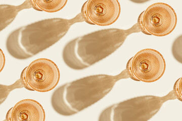 Creative pattern with white wine glasses peach color glass on beige background with hard shadows from sunlight. Summer drink concept. Trendy wine glass, vintage colored glass. Top view