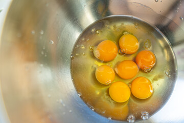 Eggs broken into a metal bowl with unbroken yolks