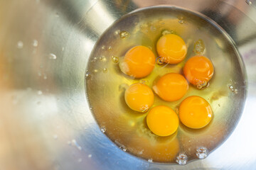 Eggs broken into a metal bowl with unbroken yolks