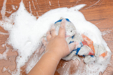 The boy washes the table with his hands with a rag.