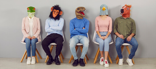 Diverse people in animal masks on head sit on chairs in line wait for interview or recruitment talk. Unknown job candidates in headmasks in queue indoors. Fun at workplace. Banner shot.