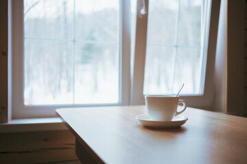 A cup on the table in front of the window.