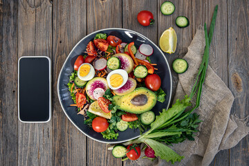 Appetizing vegetable salad with eggs, avocado on a wooden background.