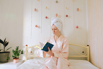 Young happy business woman with a towel on her head lies in bed in pajamas in a cozy home with notebook. Social media. Beauty routine. Skin care cosmetic concept