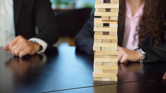 Little wooden bricks stacked up in a pile. People play jenga at the black table. Blurred background.