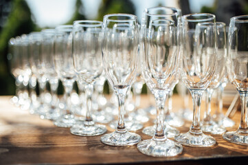 Row of empty champagne glasses on a table outdoors with sun reflection. Selective focus. Celebration concept