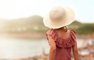 a little girl in a hat is now standing with her back to the camera on the seashore