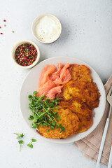 Potato pancakes. Fried homemade potato pancakes or latkes with cream, green onions, microgreens, red salmon and sauce in rustic plate on white table background. Rustic style. Healthy food. Top view.