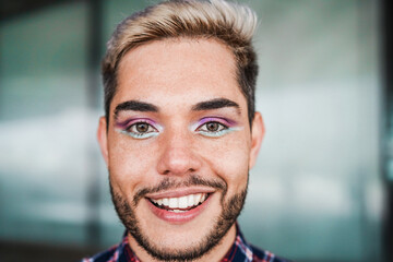 Young transgender man with makeup smiling on camera outdoor - Focus on face - obrazy, fototapety, plakaty