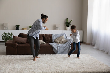 Excited active African dad and little son boy dancing on carpeted floor in living room. Father training kid, teaching, showing new dance movement, having fun, enjoying family activity