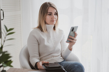 joyful charming woman using laptop and mobile phone smiling while sitting at the workplace