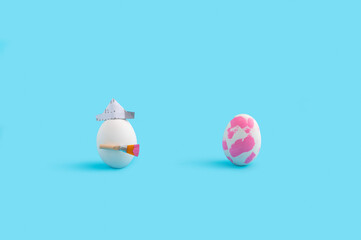 Easter concept with white egg with paintbrush and paper hat trying to paint another egg