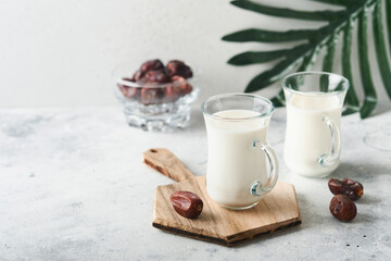 Ramadan Kareem food and drinks. Plate of dates, glass of milk and date palm branch on light grey background. Righteous Muslim Lifestyle. Place for text. Selective focus.