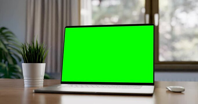 Laptop with blank green screen in home interior. Smooth camera movement around object with bokeh background. Home interior or office, 4k 30 fps UHD