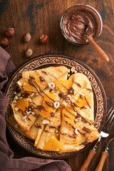 Crepes suzette with oranges and chocolate. Thin crepes with chocolate spread, hazelnuts and orange slices fruit in plate for breakfast on old dark wooden rustic table background. Copy space. Top view