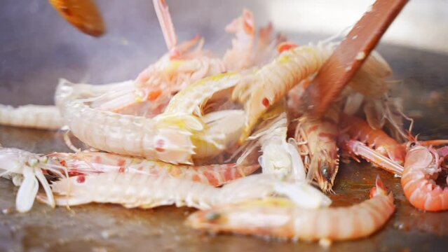 Cook or chef cooking seashells slipper lobsters in a large frying pan at the restaurant. 