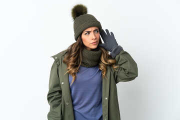 Young girl with winter hat isolated on white background listening to something by putting hand on the ear