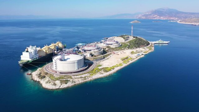 Aerial drone rotational video of LNG (Liquified Natural Gas) tanker anchored in small gas terminal island with tanks for storage