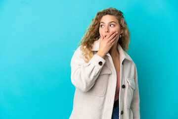 Young blonde woman isolated on blue background doing surprise gesture while looking to the side