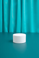 Empty podium or pedestal Mock-up for cosmetic production on a turquoise background with folds of fabric